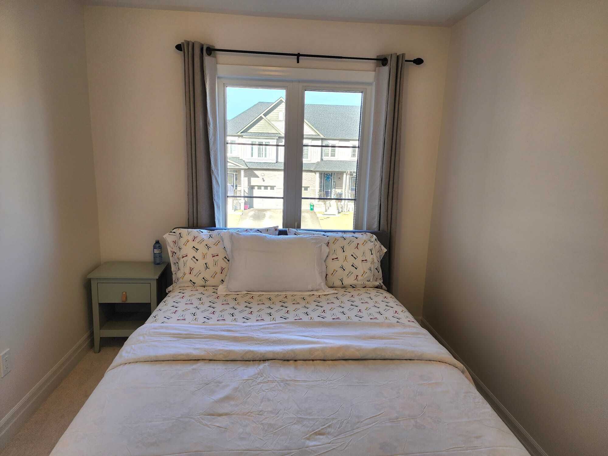 Una cama pequeña y bien hecha en una habitación de esquina con ventana.