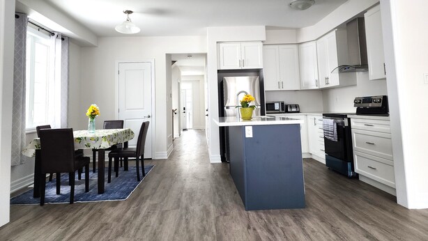 Una cocina moderna con armarios blancos, una isla central y una zona de comedor con mesa y sillas.