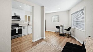 A compact kitchen with white cabinets, a black stove, and a dining area with two chairs and a small table. - Spacious Suite: Minutes to Everything! (San Diego)
