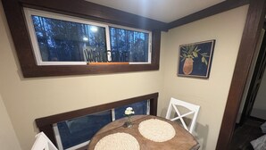 A dining area with a table, two chairs, a window with a view of trees, and a framed picture on the wall.