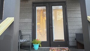 A porch with a ceiling fan, two doors with blinds, a potted plant, and outdoor furniture.