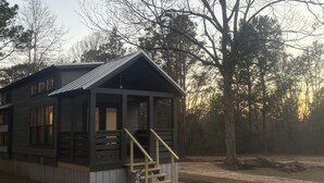 A cabin with a porch and a staircase, surrounded by trees.