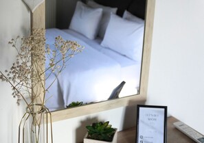 A bedroom with a bed, a bedside table with a plant, a mirror, and a framed sign.