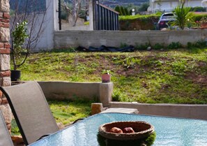 A glass table with a woven basket containing bread rolls, a brick wall, and a grassy area with a parked car in the background.