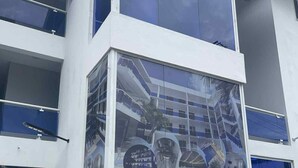Ein modernes Gebäude mit Glasfassade, mehreren Balkonen und einer zentralen Glasscheibe, die verschiedene Innenansichten zeigt.