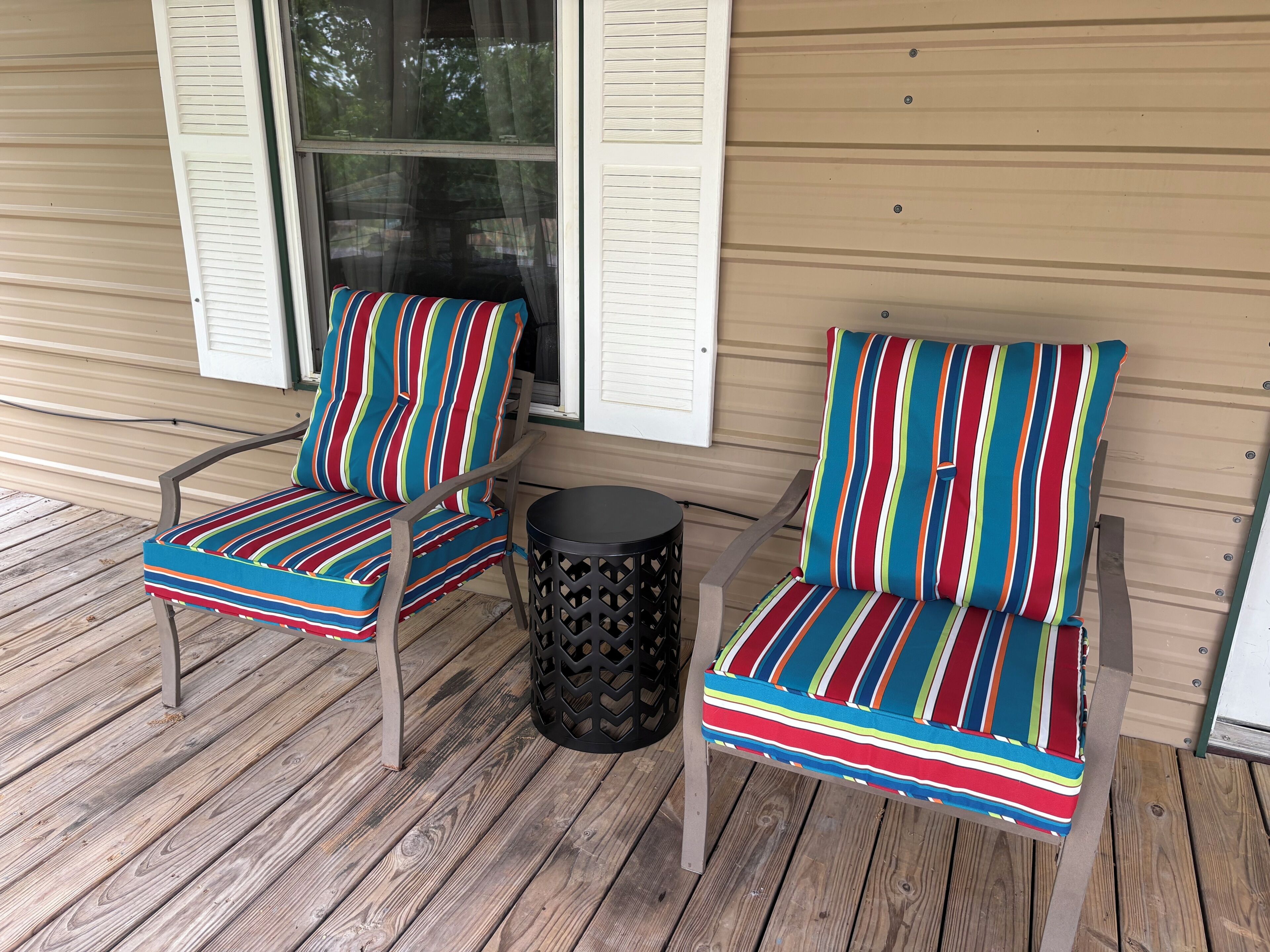 Two striped chairs with a round table on a wooden deck.