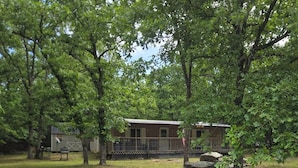 A rustic cabin surrounded by trees, with a fenced yard and a small shed. - Walk to Lake • 🔥Fire Pit • Pets Welcome 🐾.             + golf ⛳️ (Canadian)