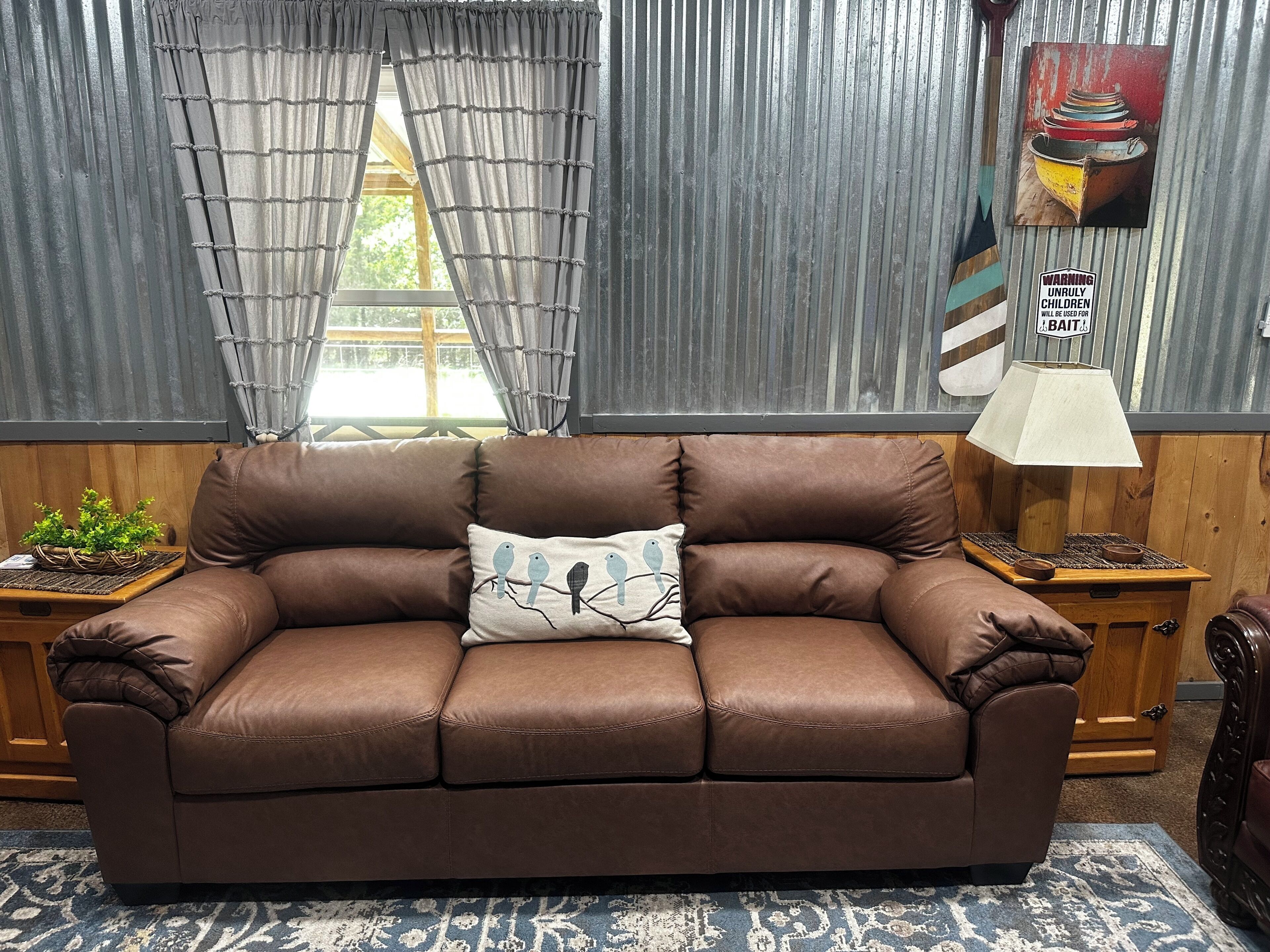 A brown leather sofa with a cushion featuring birds, a lamp, and a wall with a warning sign.