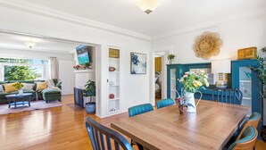 A spacious living room with a wooden dining table, blue chairs, and a green sofa. There is a TV mounted on the wall, and a large flower arrangement on the table. - King Bed Comfort Ultra Spacious Gem Prime Location south pasadena! (South Pasadena)
