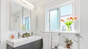 A modern bathroom with a white sink, dark cabinets, a large mirror, and a window with a view of buildings. - King Bed Comfort Ultra Spacious Gem Prime Location south pasadena! (South Pasadena)