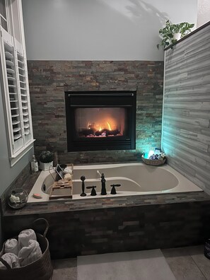 A bathroom with a stone wall, a fireplace, a bathtub, and a window with blinds. - Spacious 4-bedroom4bth house in private golf course community ready for Masters (North Augusta)