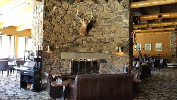 A lobby with a stone wall, a mounted deer head, a fireplace, and seating areas. - Sunshine Mountain Lodge - Superior Room (Banff)