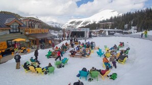 An outdoor seating area with chairs and tables, surrounded by buildings and snow-covered mountains. - Sunshine Mountain Lodge - Superior Room (Banff)