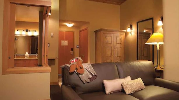 A cozy living room with a leather sofa, a wooden cabinet, and a mirror. - Sunshine Mountain Lodge - Superior Room (Banff)