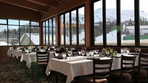 A restaurant with tables set for dining, large windows with a mountain view, and a carpeted floor. - Sunshine Mountain Lodge - Superior Room (Banff)