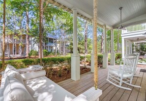 A covered outdoor seating area with white furniture, a swing, and a view of surrounding buildings. - WaterColor-Golf cart-5 Bikes & Resort Amenities  (Santa Rosa Beach)