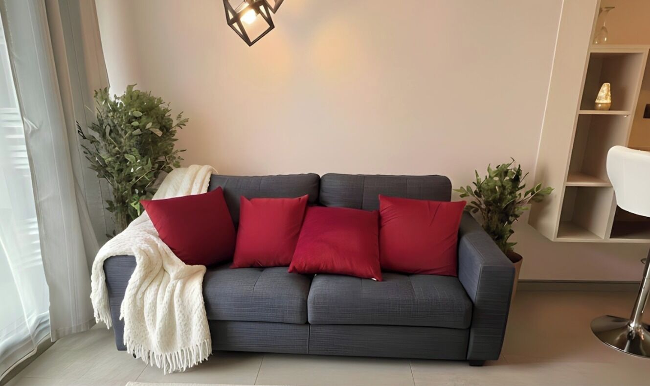 A grey sofa with red cushions, a white throw blanket, and two potted plants.