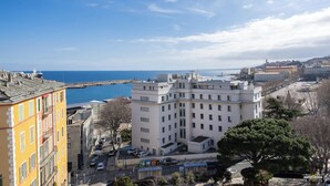 Un paysage urbain côtier avec un grand bâtiment blanc qui domine le centre, entouré d’autres bâtiments et offrant une vue dégagée sur la mer.
