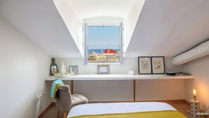 Une chambre avec une lucarne, un lit, un bureau avec un ordinateur et une vue sur la plage.