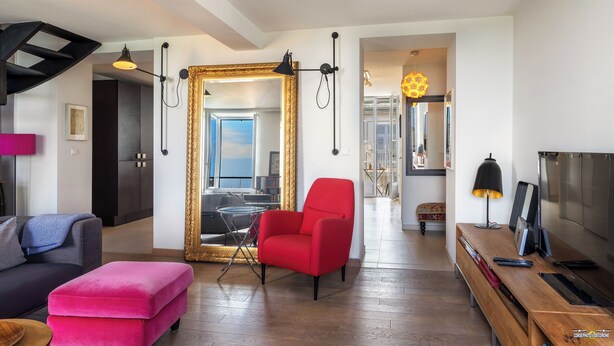 Un salon spacieux avec un fauteuil rouge, un grand miroir et une table basse en bois.