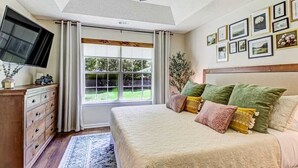 A bedroom with a large bed, a dresser, a television, and a window with curtains. - NEW TO VRBO SPECIAL! 4 Bedroom Home- 6 mi to Airport, 11 mi to Downtown (Pooler)