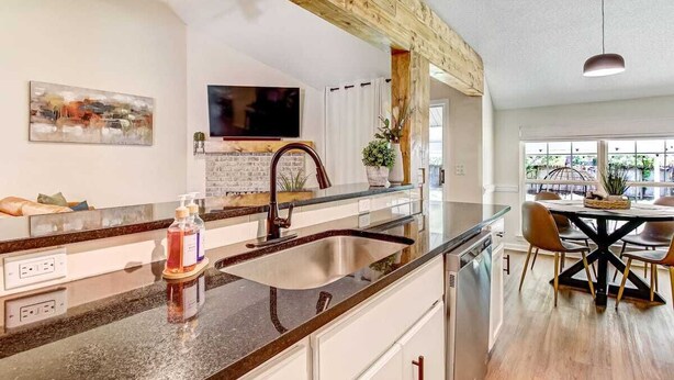 A modern kitchen with a granite countertop, stainless steel sink, and a dining area with a black table and chairs. - NEW TO VRBO SPECIAL! 4 Bedroom Home- 6 mi to Airport, 11 mi to Downtown (Pooler)