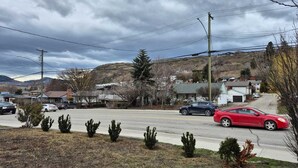 Une rue résidentielle bordée de maisons, avec une voiture rouge et une colline en arrière-plan.