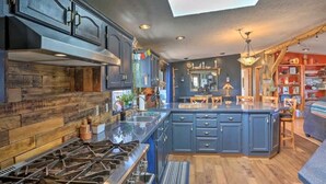 A modern kitchen with a central island, dark cabinetry, and a large window. - Cozy Black Hills Home on 13 Acres w/ Deck & Views!! (Hot Springs)