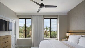 Une chambre d’hôtel avec un lit, une télévision, un bureau et une fenêtre donnant sur des palmiers.