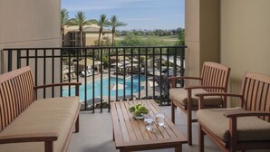 Un balcon avec vue sur la piscine, des meubles en bois et une table avec un saladier de fruits et des verres.