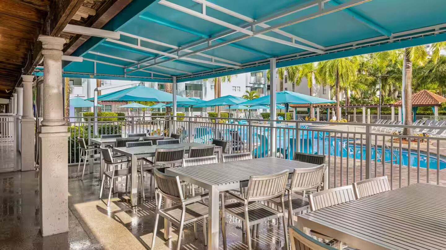 An outdoor patio area with tables and chairs, a pool, and umbrellas.