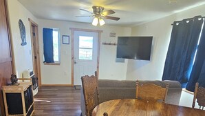 A dining area with a wooden table and chairs, a ceiling fan, and a television on the wall. - Mountain Crest Cabin - Cozy Lodging, Close to Cody (Cody)