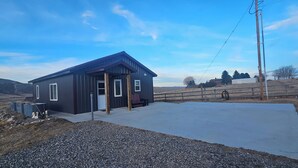 A modern building with a dark exterior, a concrete patio, and a wooden fence. - Mountain Crest Cabin - Cozy Lodging, Close to Cody (Cody)