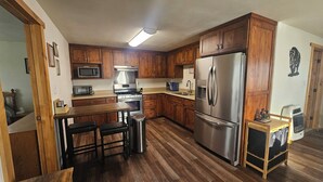 A kitchen with wooden cabinets, stainless steel appliances, a microwave, a stove, and a refrigerator. - Mountain Crest Cabin - Cozy Lodging, Close to Cody (Cody)