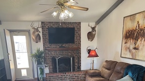 Ein Wohnzimmer mit Kamin, Ledersofa, Holzboden und Deckenventilator.