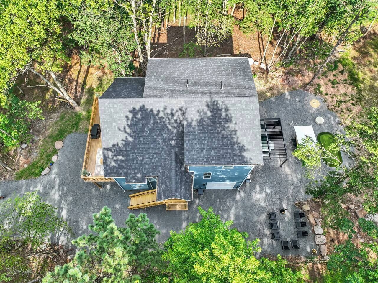 A two-story building with a flat roof, surrounded by trees. There is a paved area with outdoor seating and a small pool.