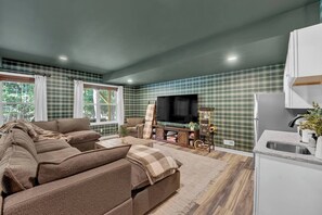 Ein Wohnzimmer mit einer Couch, einem Fernseher und einer kleinen Küchenzeile mit einem Kühlschrank.