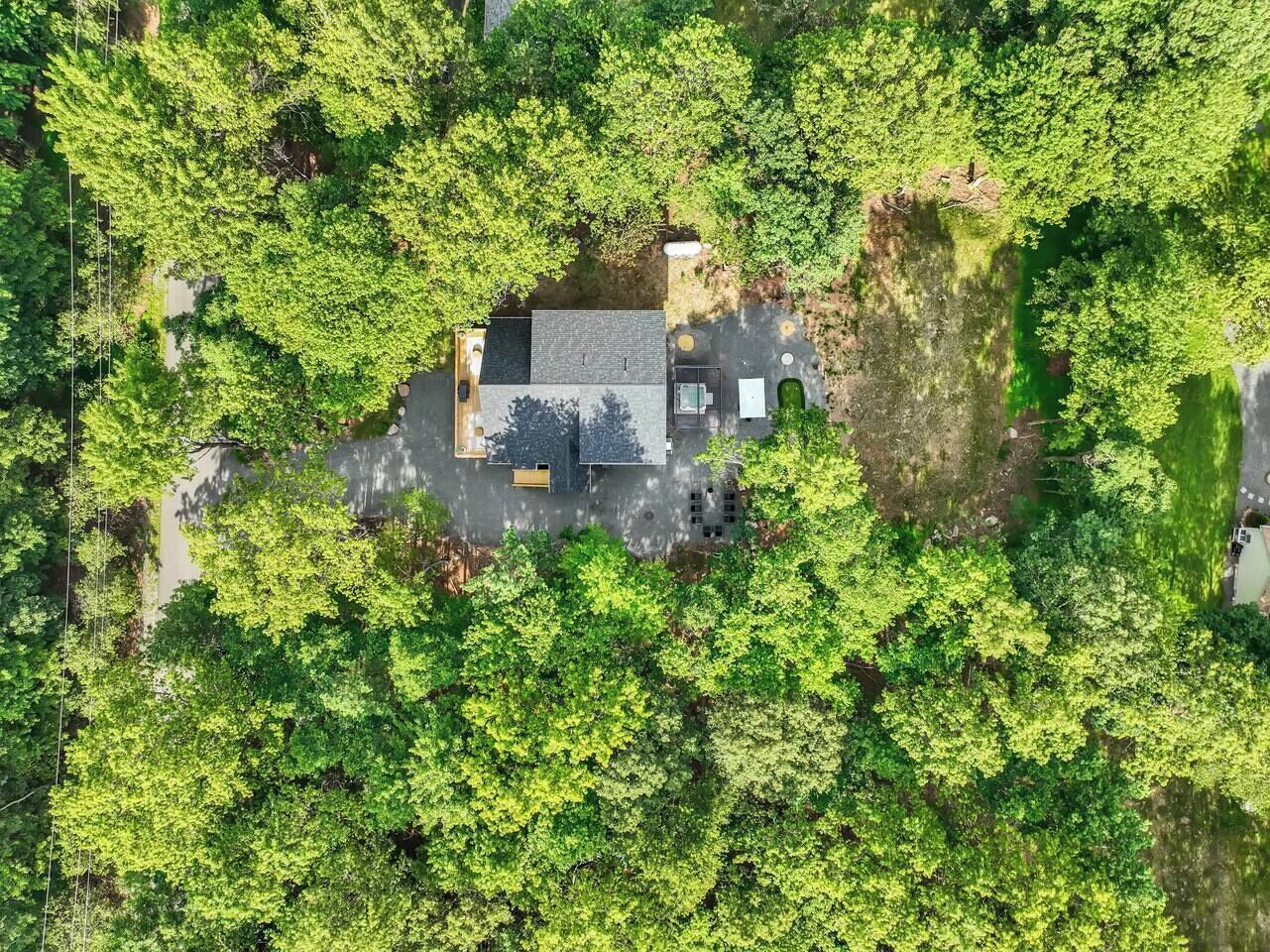 An aerial view of a house surrounded by dense greenery, with a paved driveway and a small patio area.