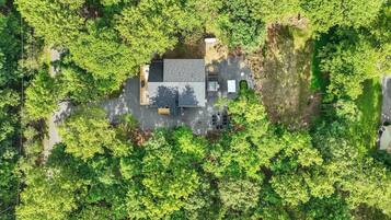 An aerial view of a house surrounded by dense greenery, with a paved driveway and a small patio area.