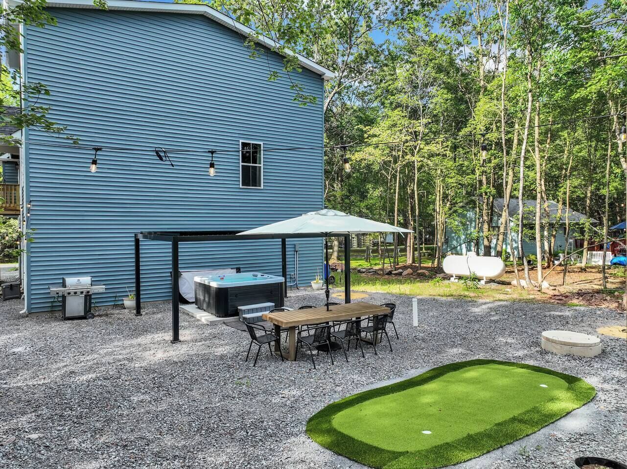 A blue building with a covered patio, outdoor grill, and hot tub.