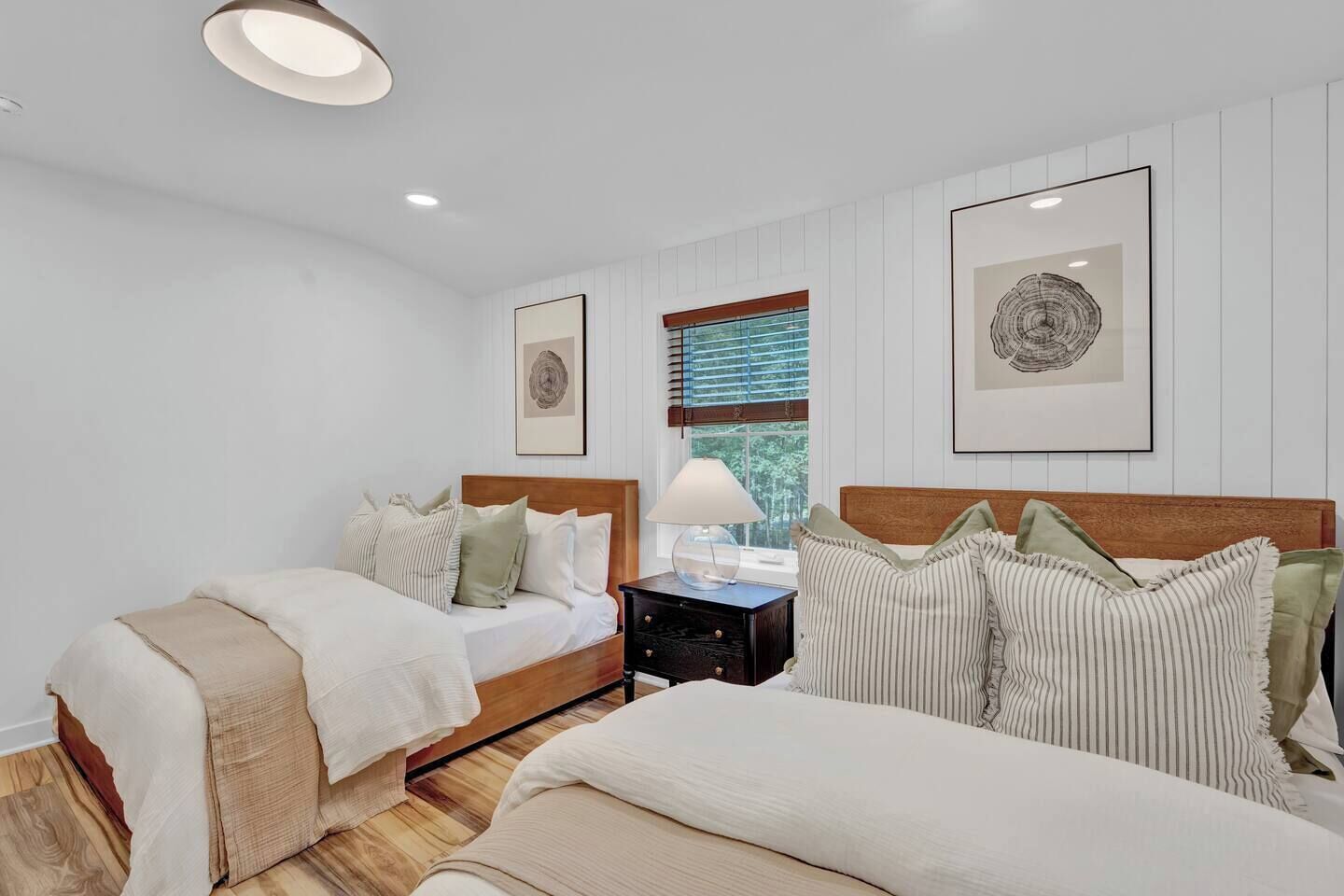 A bedroom with two beds, a nightstand, and framed artwork on the walls.