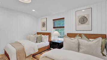 A bedroom with two beds, a nightstand, and framed artwork on the walls.