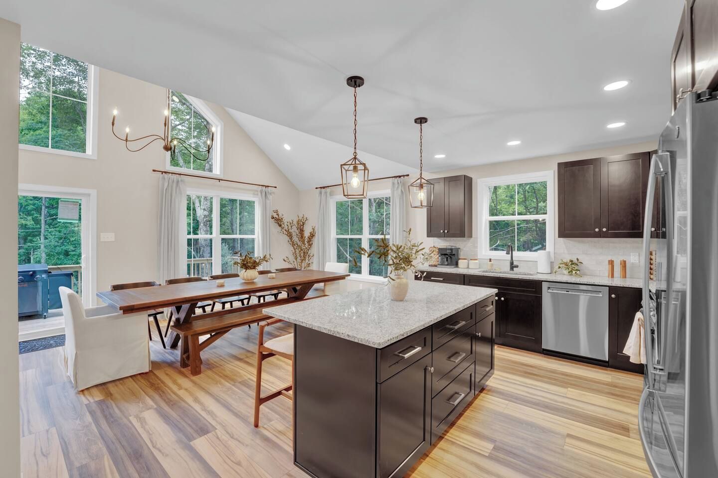 A modern kitchen with a large island, dark cabinetry, and a view of the outdoors.