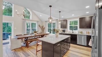 A modern kitchen with a large island, dark cabinetry, and a view of the outdoors.