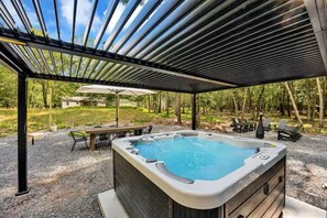 Lämmitetty poreallas, jonka yläpuolella on pergola. Lähellä on pöytä ja tuoleja, ja aluetta ympäröi kivimurskepintainen alue sekä puita.