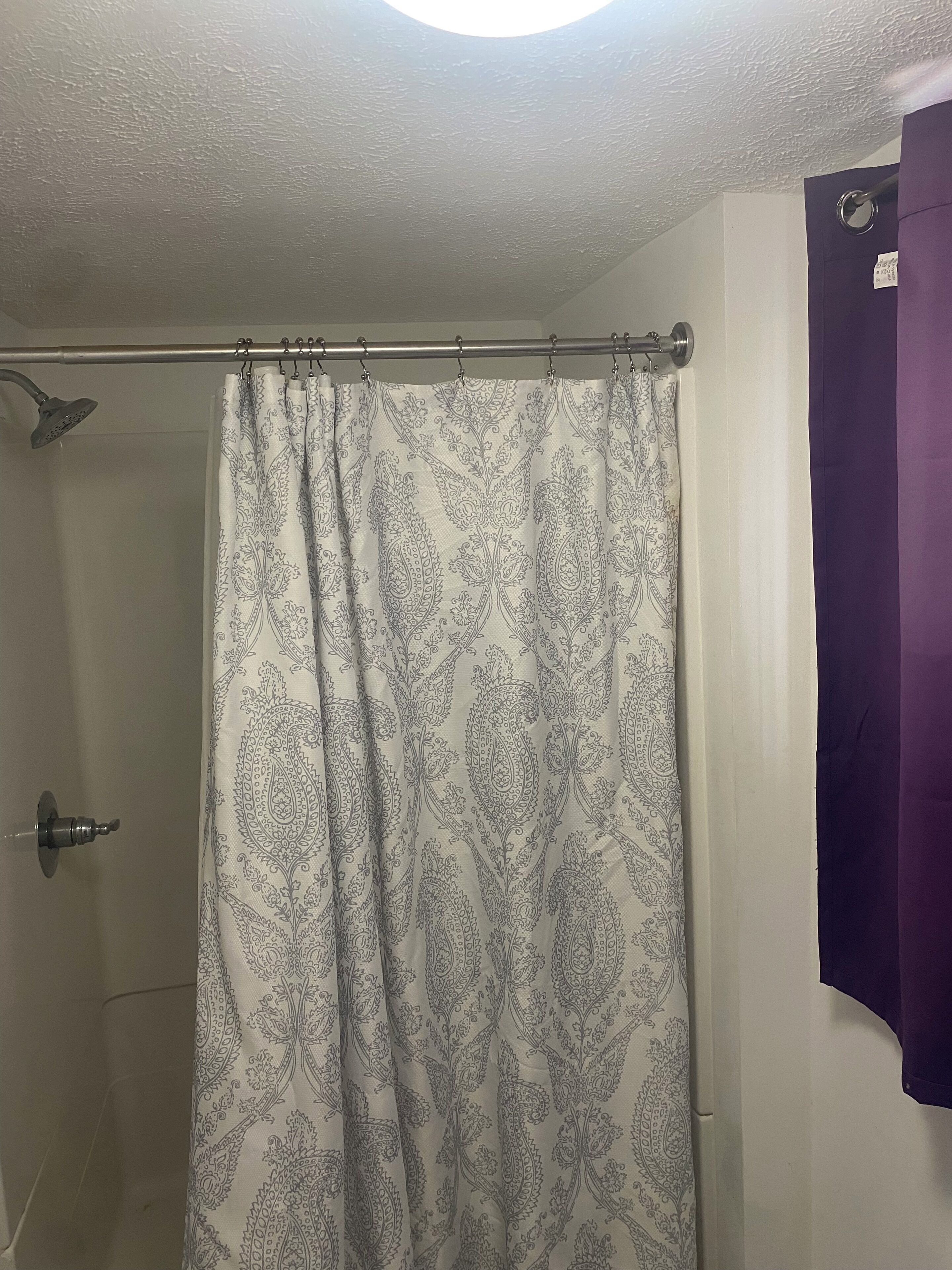 A shower area with a patterned shower curtain, a showerhead, and a purple curtain on the right.