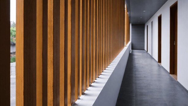 A corridor with wooden slats on one side and a dark floor, leading to a series of doors. - Miracle Hotel Cianjur (Cianjur)