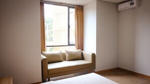 A room with a beige sofa, a window with curtains, and an air conditioning unit on the wall. - Miracle Hotel Cianjur (Cianjur)
