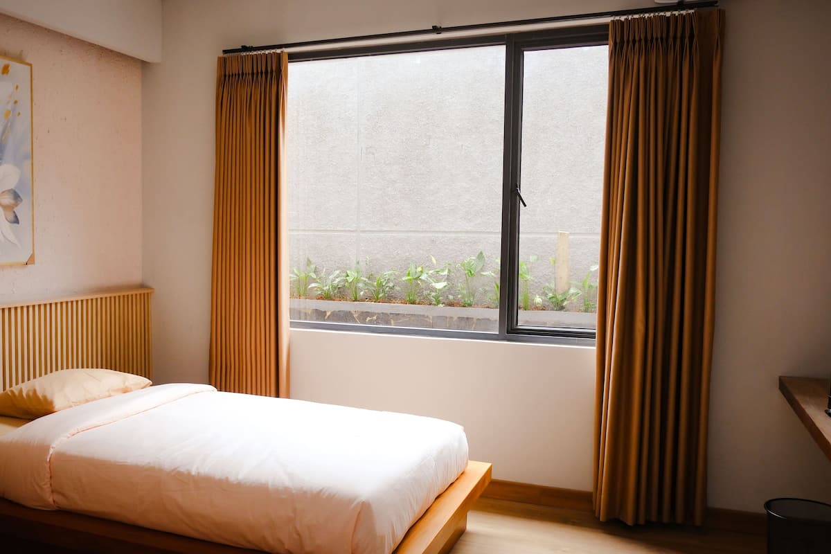 Une chambre d’hôtel avec un lit, une table de chevet, une fenêtre avec des rideaux et un radiateur fixé au mur.
