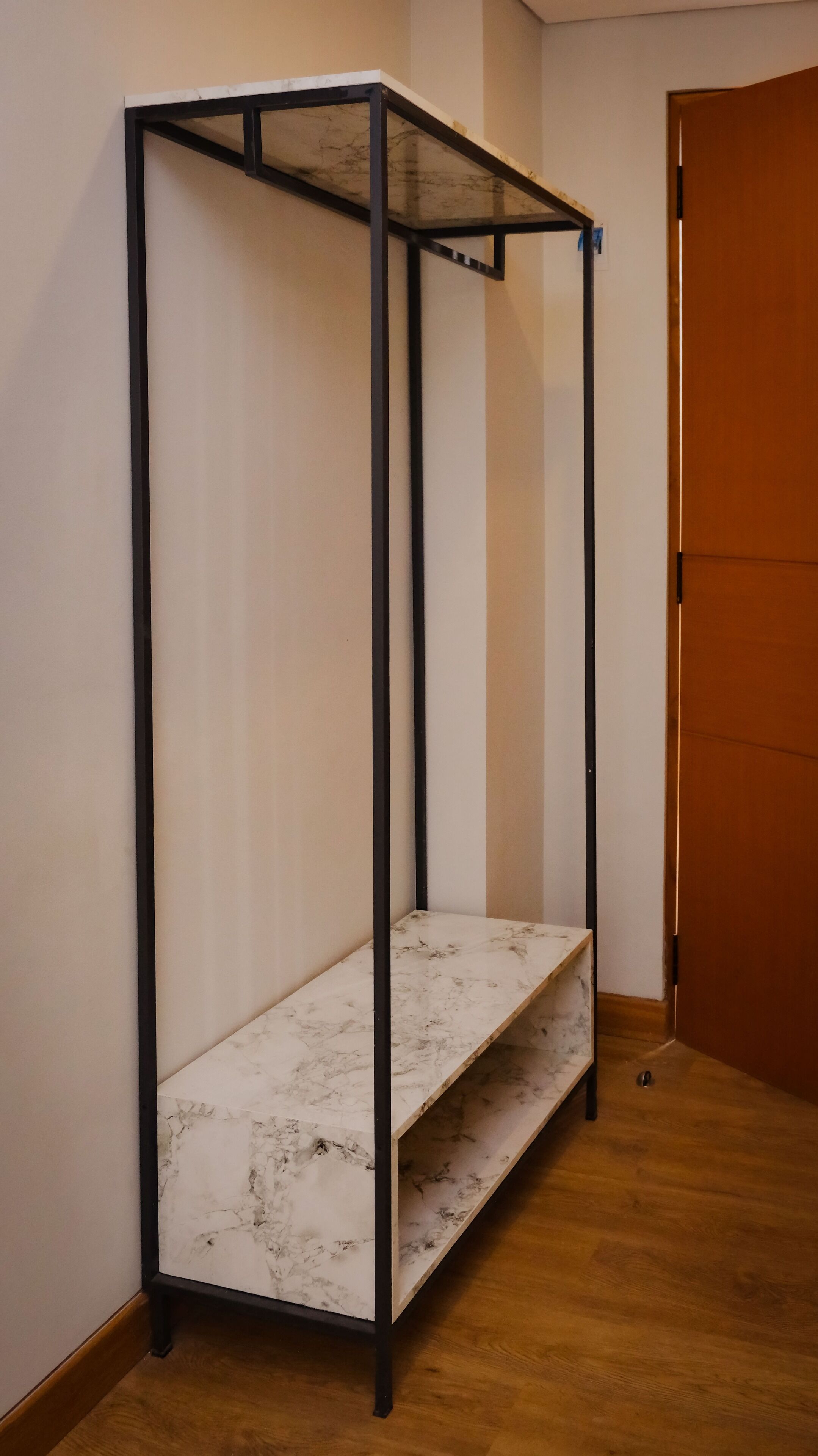 A corner room with a metal-framed shelving unit against the wall, a wooden door, and a wooden floor.